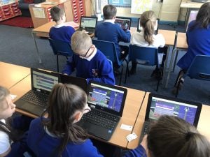 Photo of school children in a classroom playing TT Rock Stars on laptops.